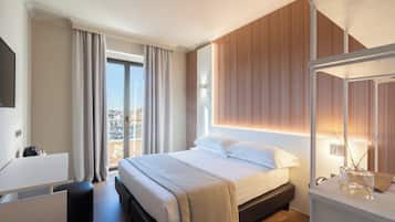 Een moderne hotelkamer met een groot bed, een bureau, een stoel en uitzicht op de stad door het raam.