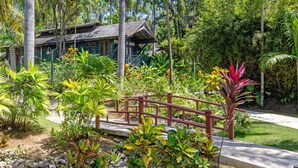 A tropical resort with a wooden bridge, lush greenery, and a building with a dark roof. - Sunset at the Palms Resort - Adults Only - All Inclusive (Negril)