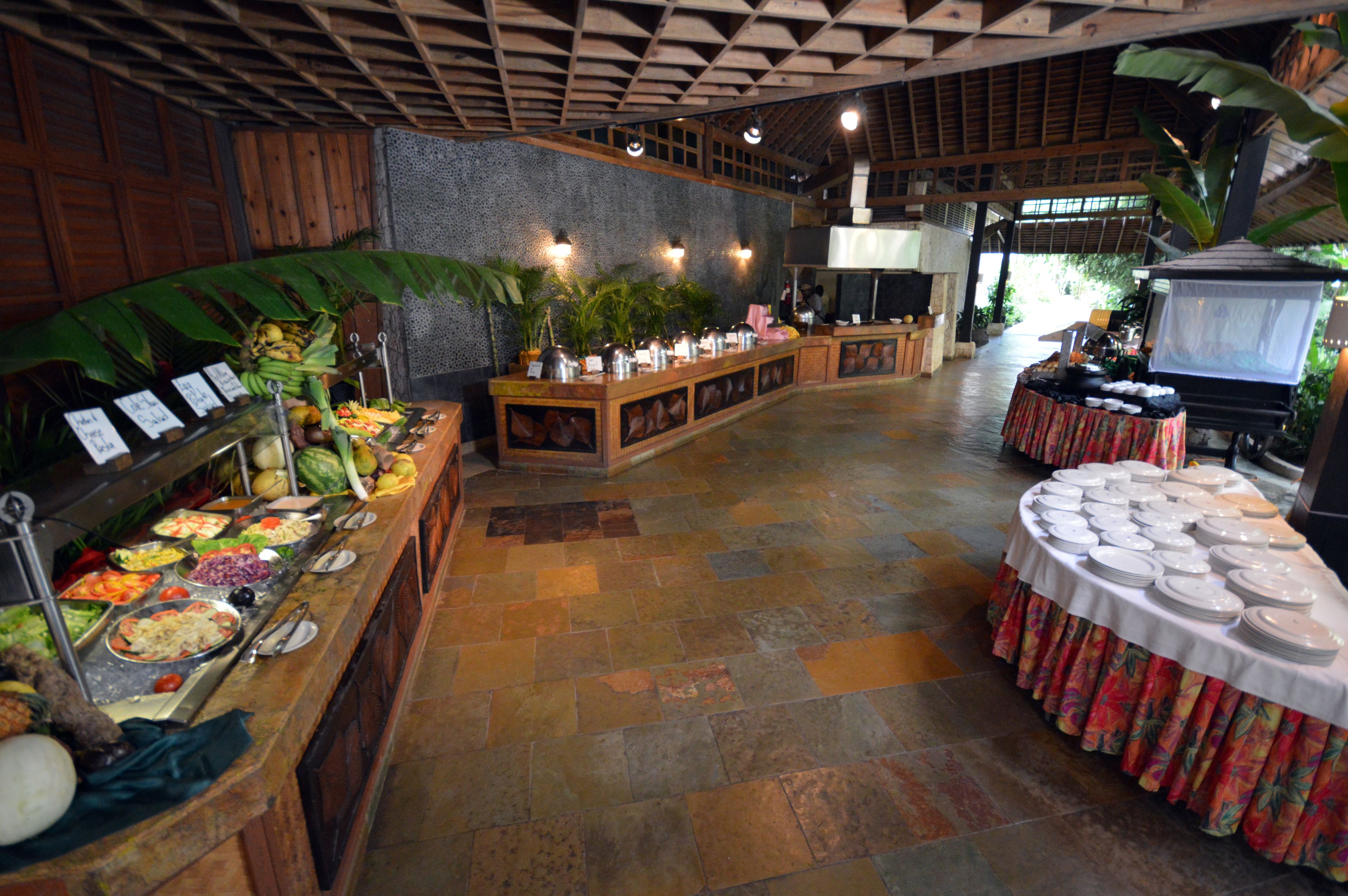 A buffet area with various food stations, a central serving counter, and a seating area with tables set for dining.