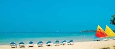 Een privéstrand, wit zand, ligstoelen aan het strand, parasols