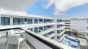 A modern hotel balcony with glass railings, white furniture, and a view of the pool area. - Apartamentos Vibra Jabeque Blue - Adults only (Ibiza Town)