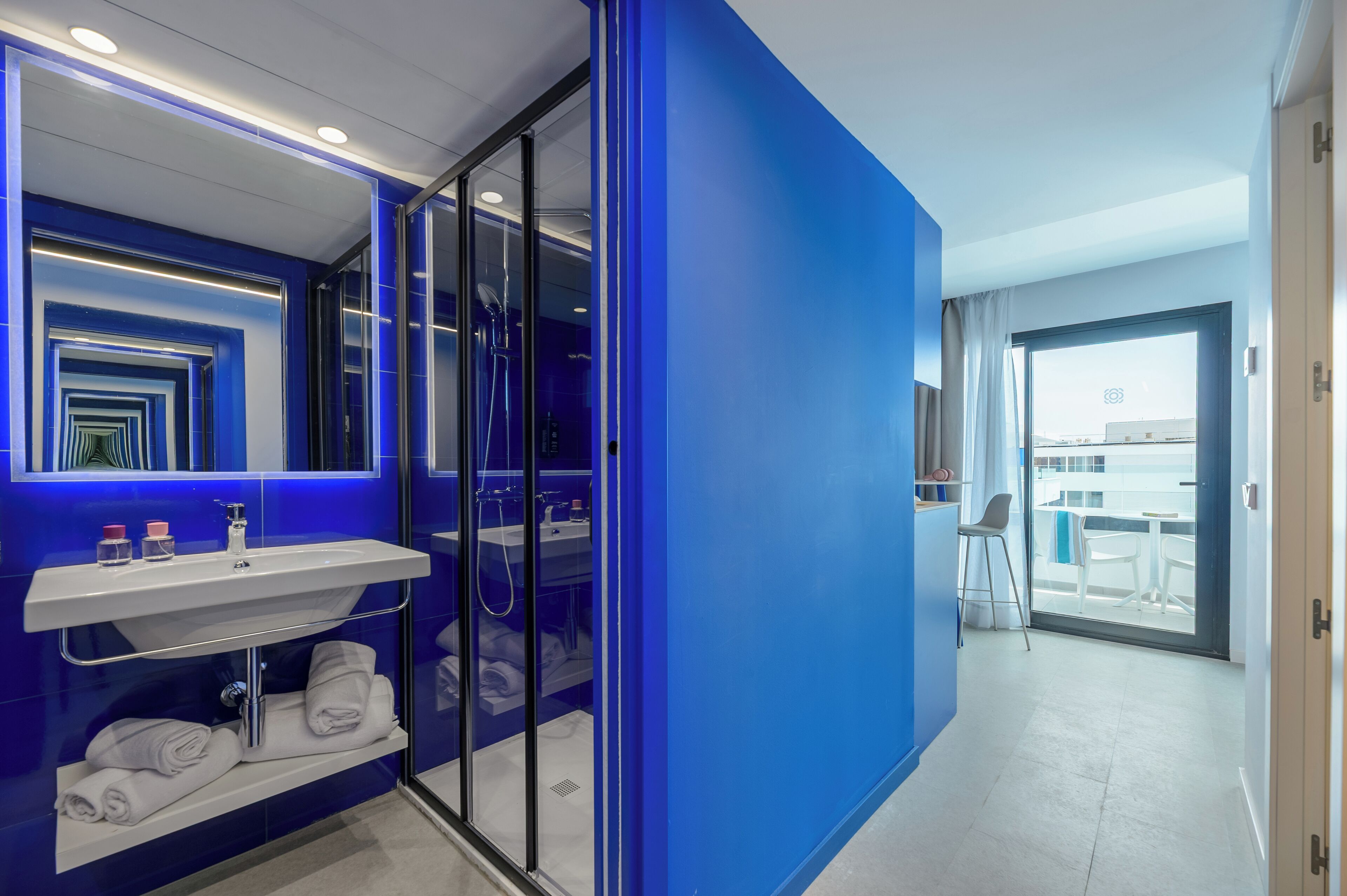 A modern bathroom with a blue accent wall, a glass shower enclosure, a white sink, and a towel rack.