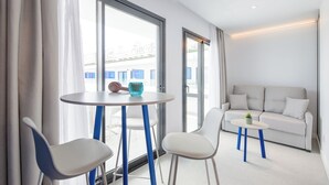 A modern hotel room with a round table, two chairs, a sofa, and a large window with curtains. - Apartamentos Vibra Jabeque Blue - Adults only (Ibiza Town)