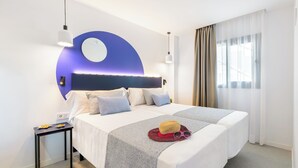 A modern hotel room with a large bed, a bedside table, a wall-mounted circular light, and a window with sheer curtains. - Apartamentos Vibra Jabeque Blue - Adults only (Ibiza Town)