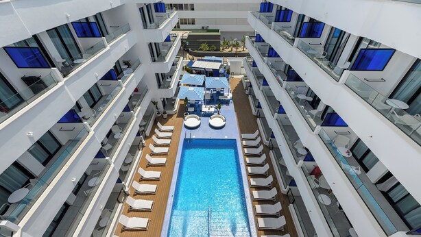 A multi-level pool area with sun loungers and umbrellas, surrounded by balconies with glass railings. - Apartamentos Vibra Jabeque Blue - Adults only (Ibiza Town)