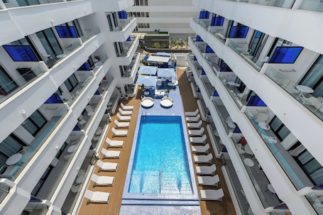 A multi-level pool area with sun loungers and umbrellas, surrounded by balconies with glass railings.