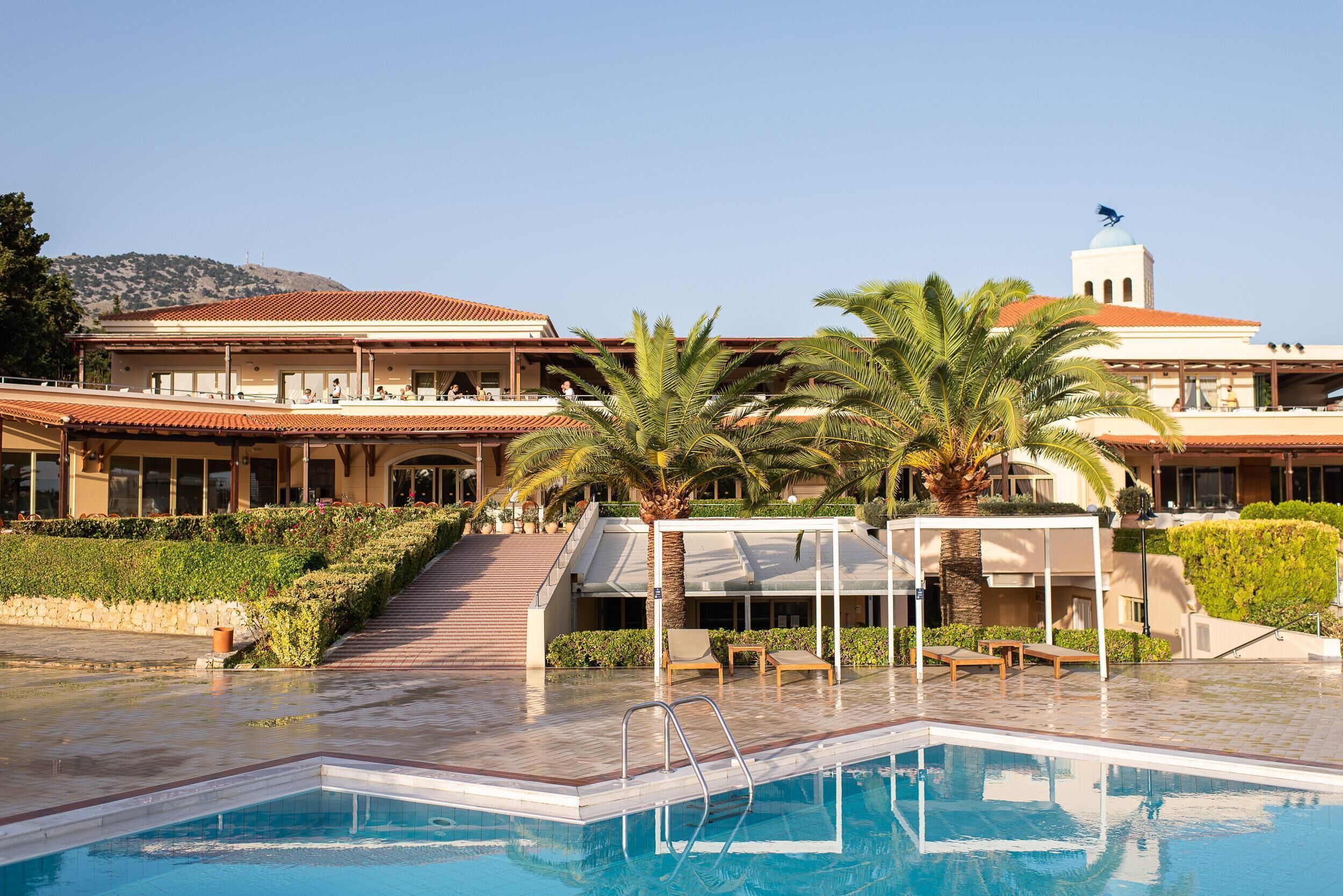 Ein Resort mit Swimmingpool, Palmen und einem Gebäude mit rotem Ziegeldach.