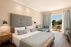 A hotel room with a large bed, two bedside tables, a sofa, and a balcony with a view of palm trees.