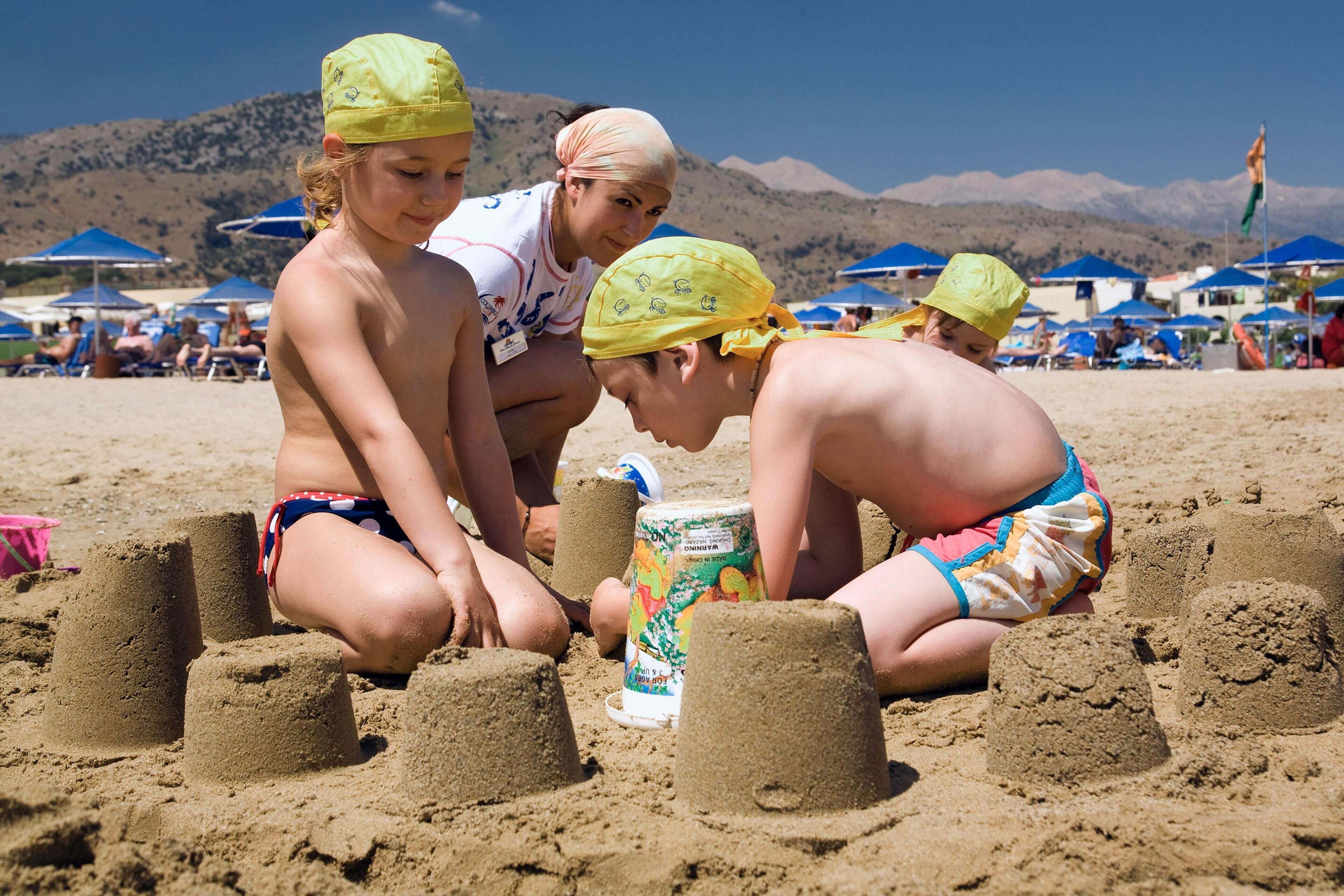 Bambini che costruiscono castelli di sabbia su una spiaggia, con montagne sullo sfondo.