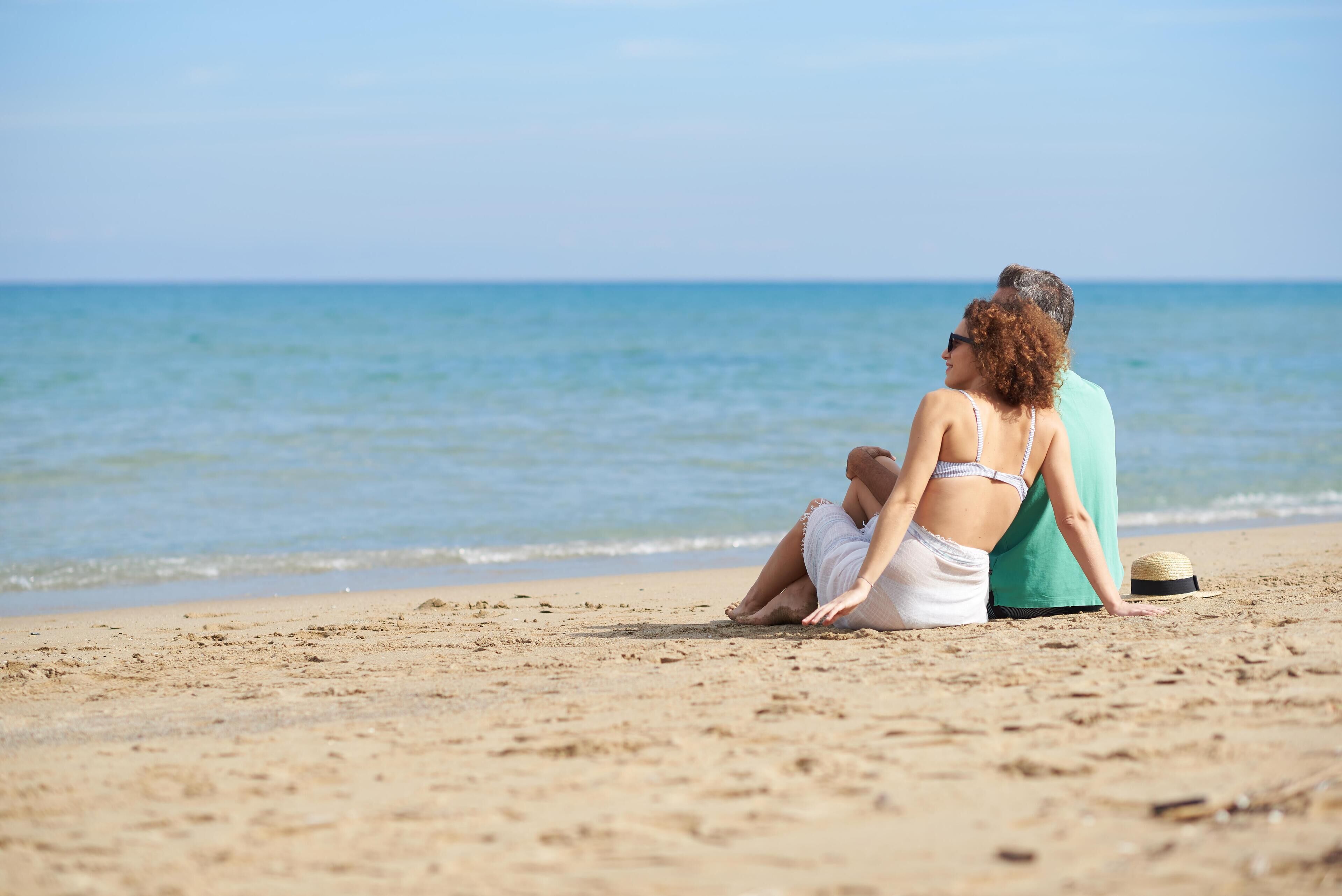 Two people sitting on a sandy beach with the ocean in the background.