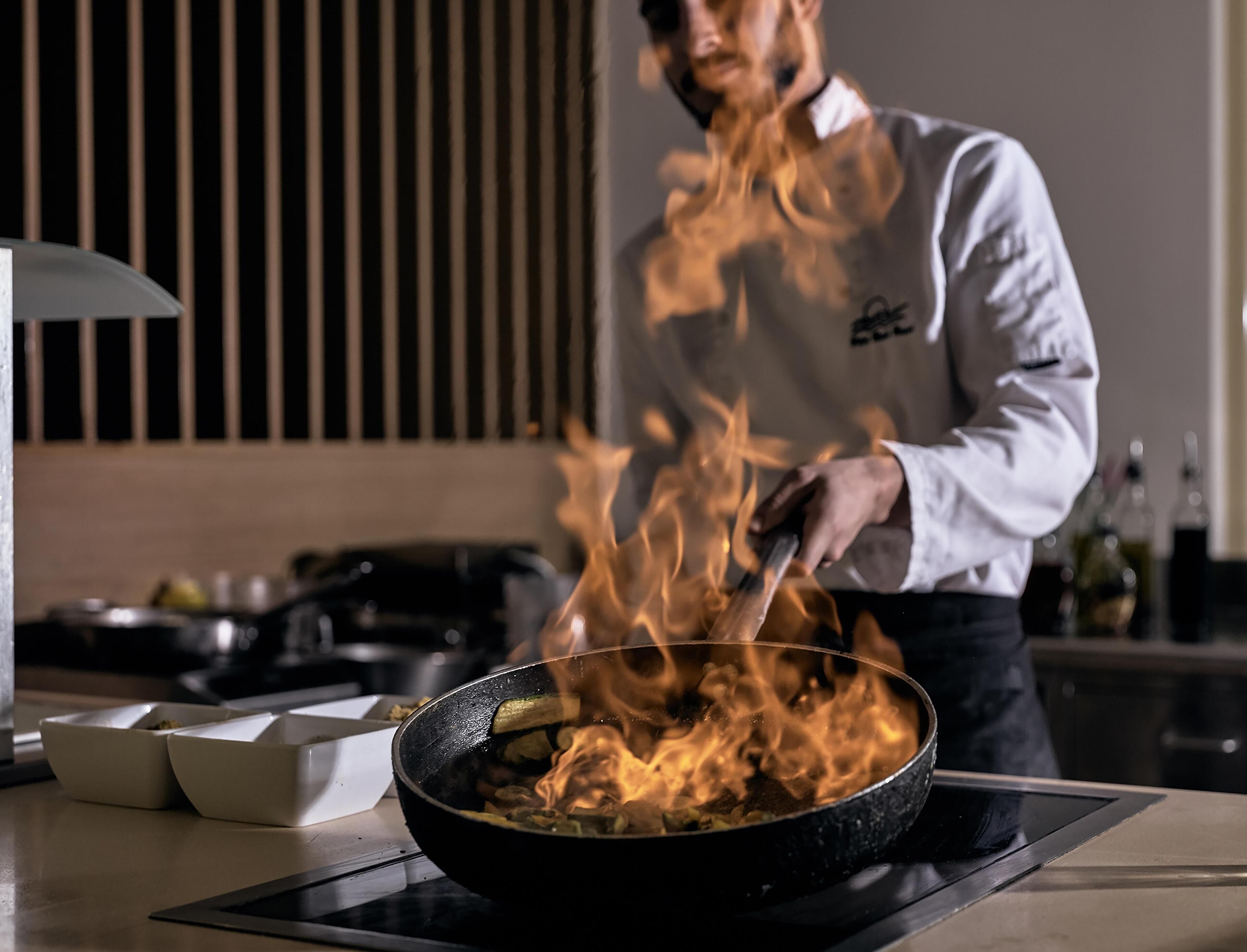 Un cocinero cocinando sobre fuego en una sartén.