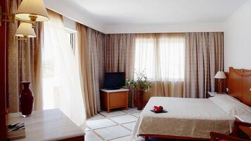 Una habitación de hotel con una cama, televisión, escritorio y un florero con flores.