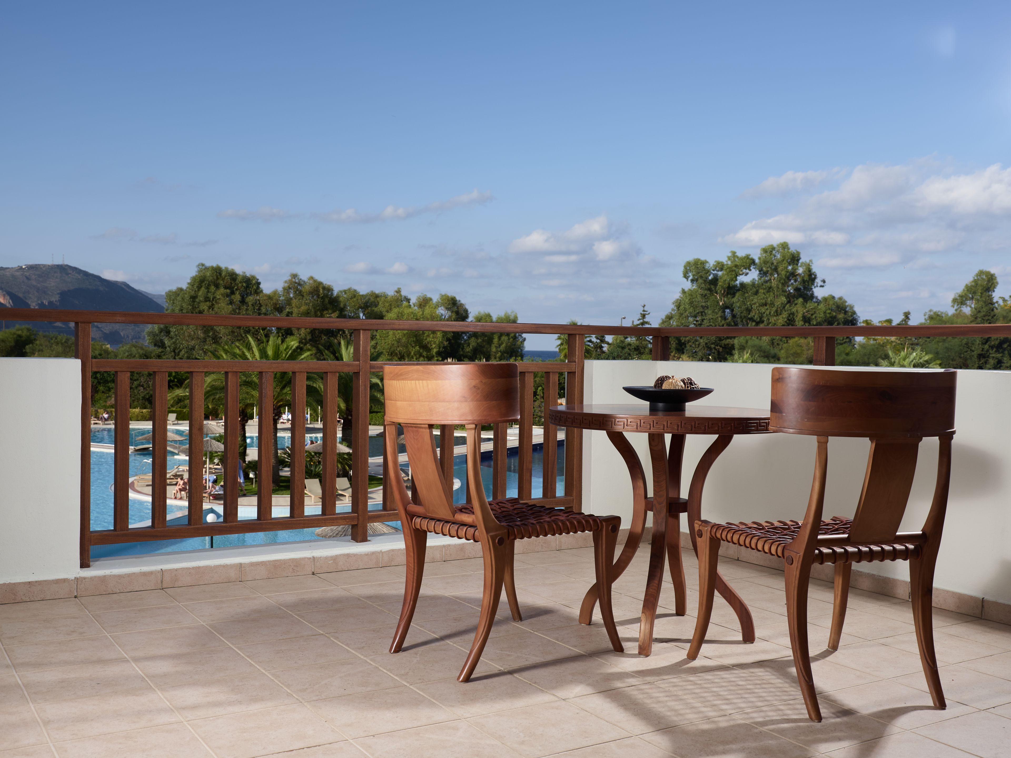 Ein Balkon mit zwei Holzstühlen und einem Tisch, mit Blick auf einen Pool und üppige Vegetation.