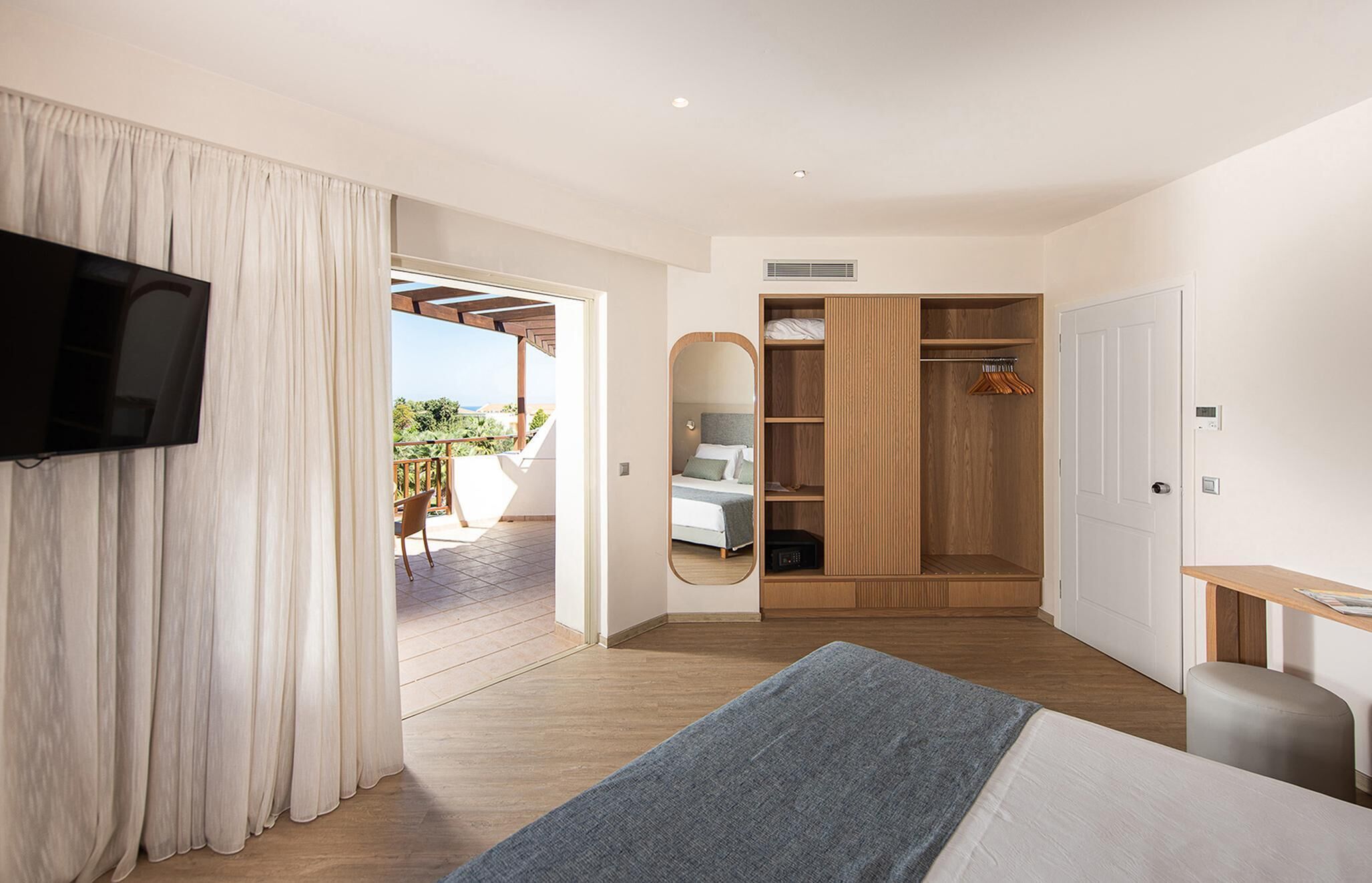 A modern hotel room with a large bed, a TV, a wooden wardrobe, and a balcony with a view.