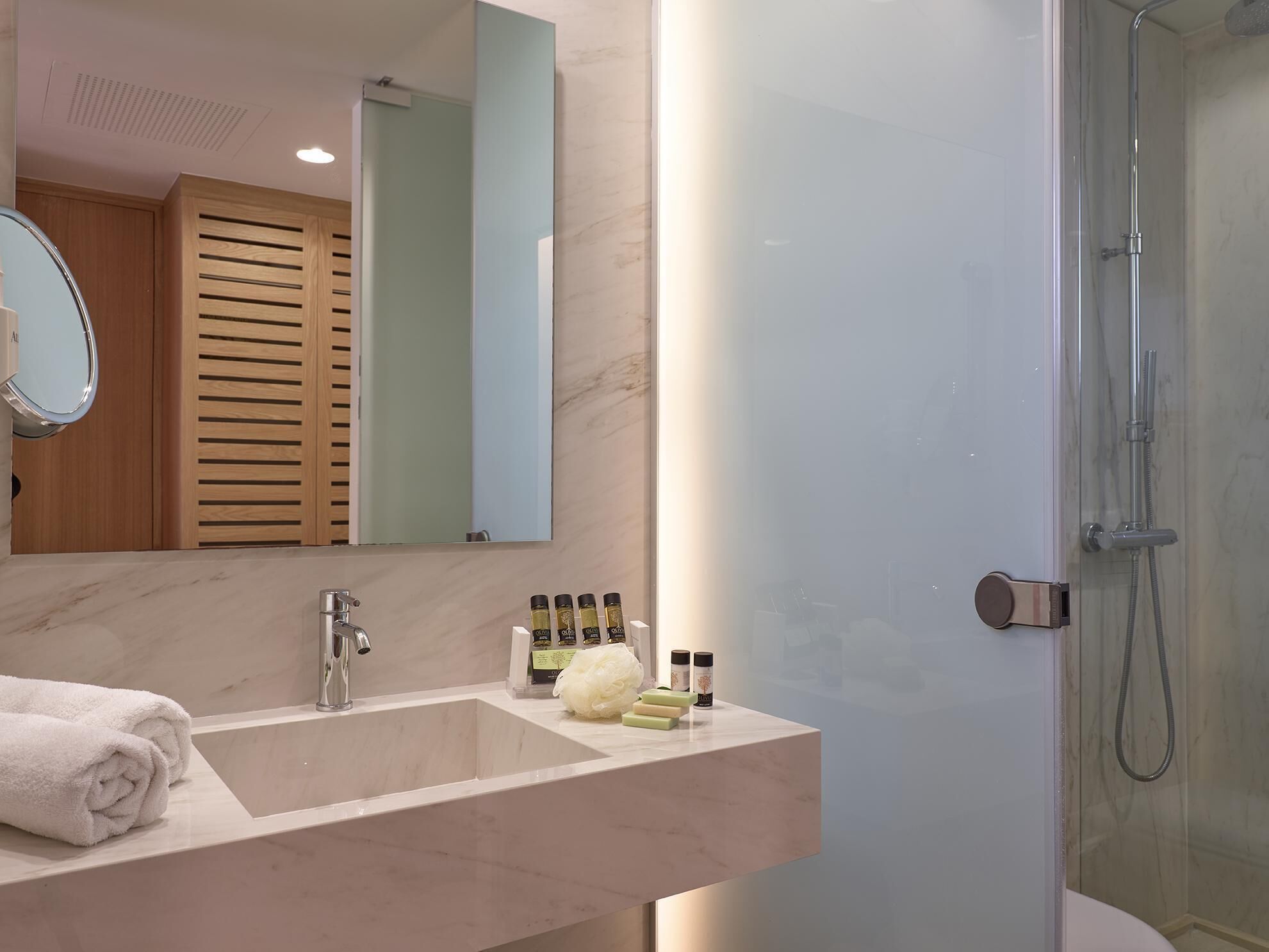 Un baño moderno con lavamanos de mármol, un espejo grande y una ducha con paredes de vidrio.