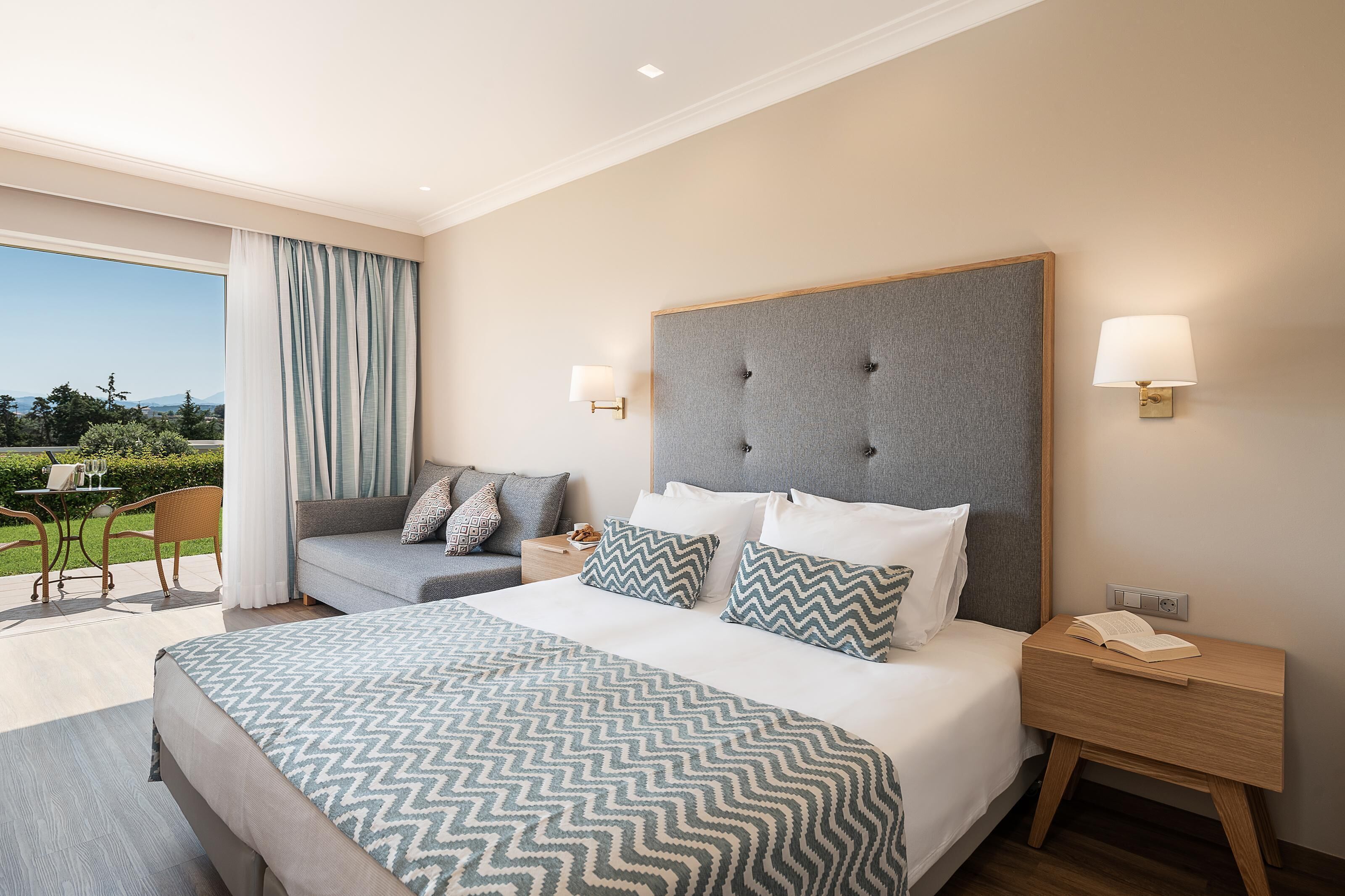 Habitación de hotel con una cama grande, dos mesitas de noche, un sofá y vistas al exterior.