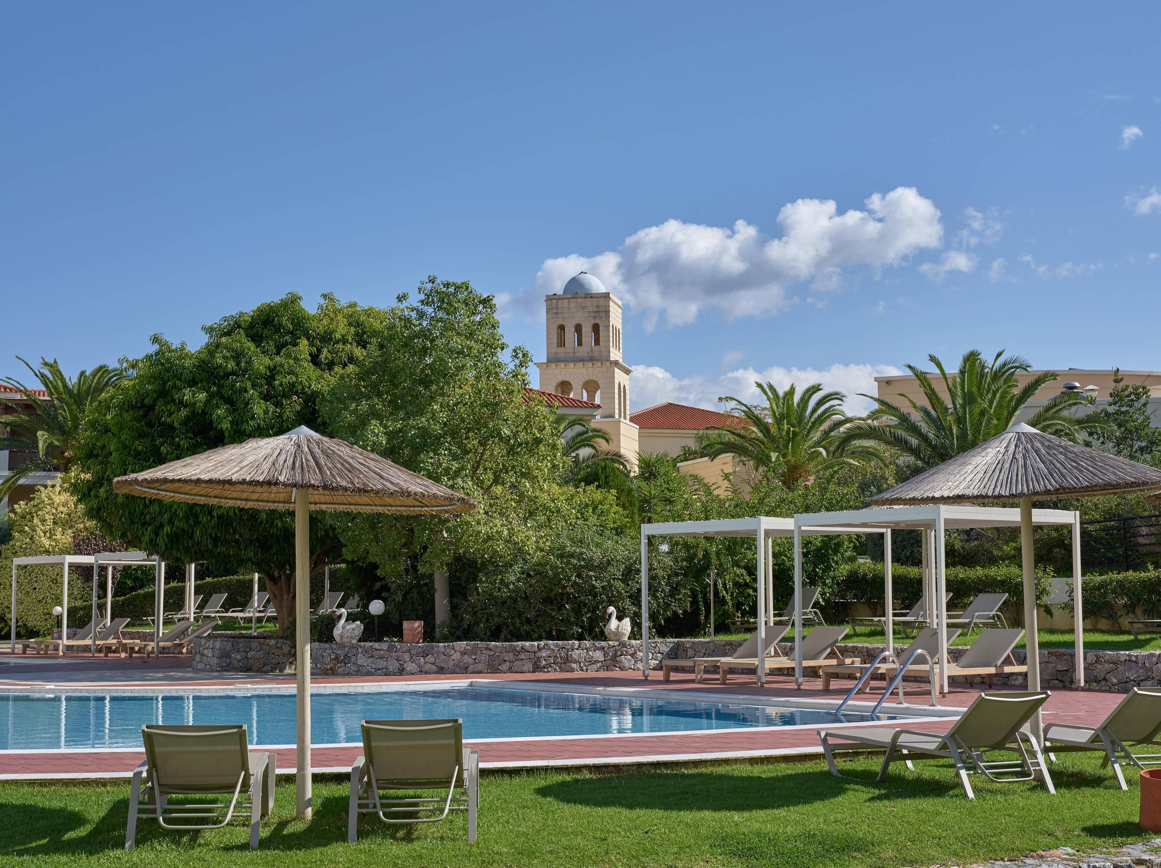 A pool area with lounge chairs, umbrellas, and a building with a tower in the background.