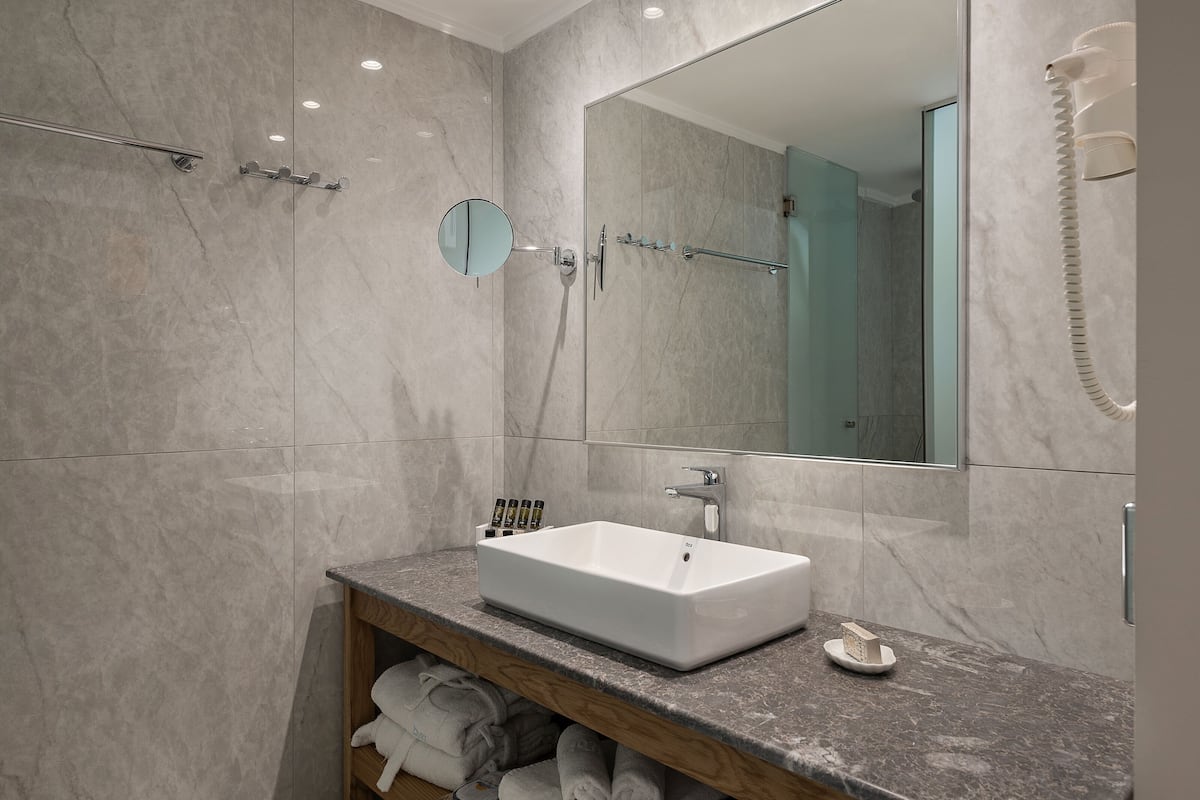 Un baño moderno con un espejo grande, un lavamanos blanco y una ducha con mampara de vidrio.