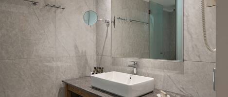 A modern bathroom with a large mirror, a white sink, and a glass-enclosed shower.