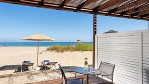 Un patio frente a la playa con terraza de madera, mobiliario exterior y vistas al mar.