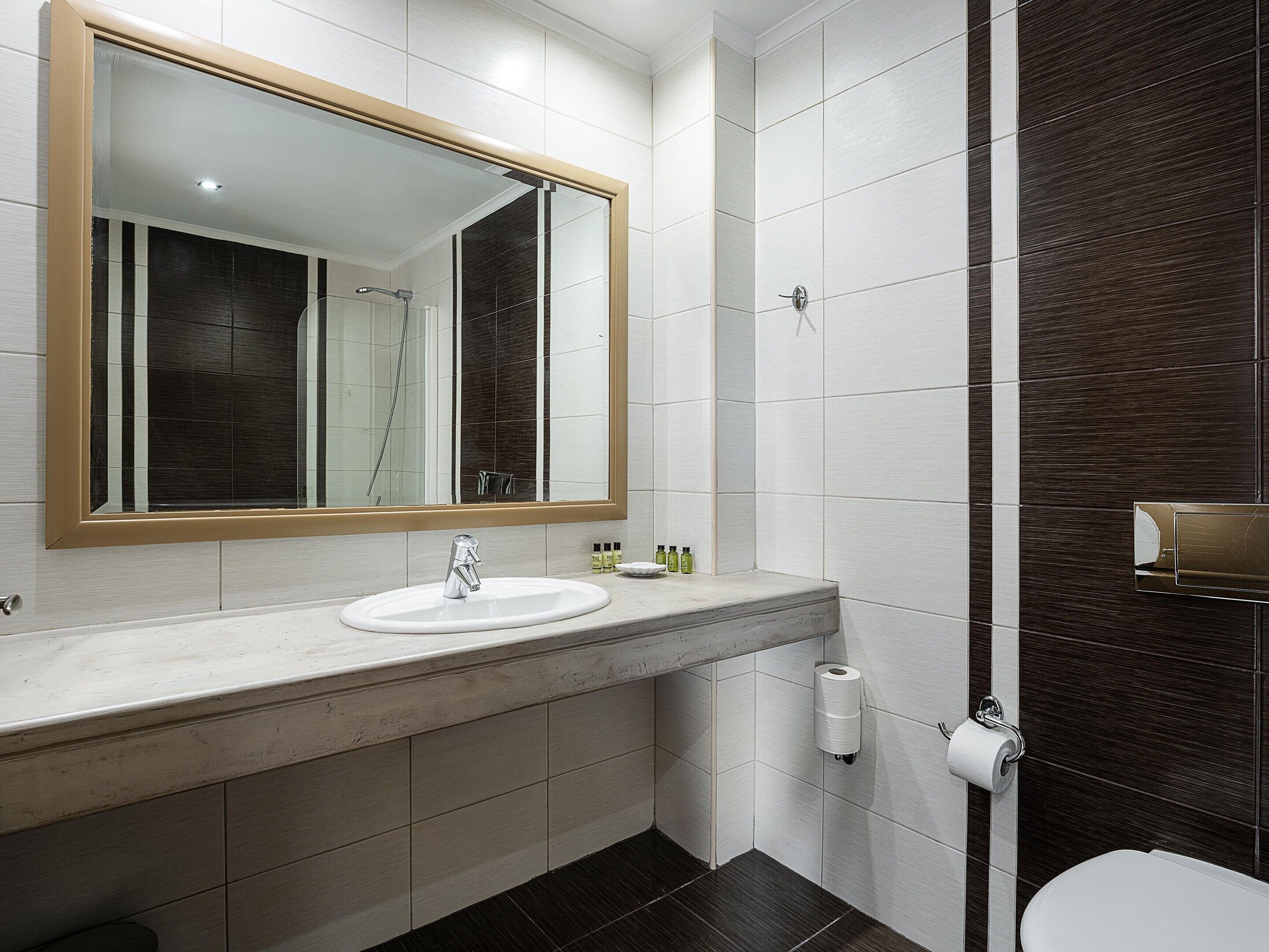 A modern bathroom with a large mirror, a sink, a toilet, and a shower area.