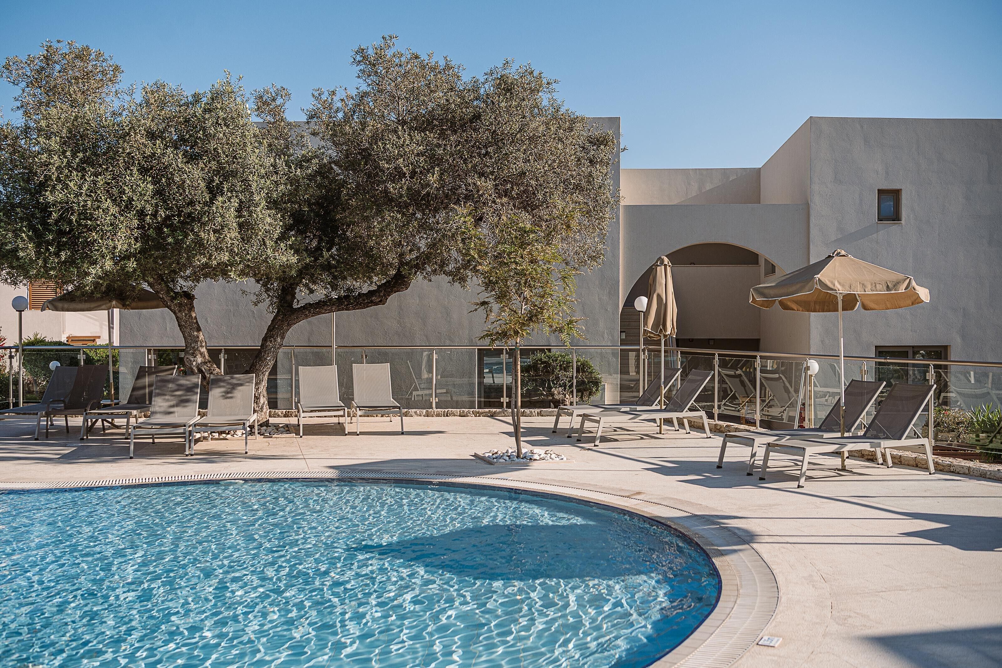 A swimming pool with lounge chairs and umbrellas, surrounded by a building with a modern architectural style.