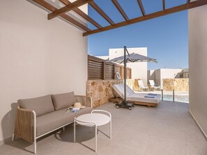 A sunlit outdoor seating area with a sofa, two chairs, a table, and a poolside lounge with umbrellas. - Sirios Village Hotel & Bungalows - All Inclusive (Chania)
