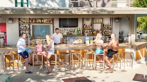 Zona de bar con varias opciones de asientos, una variedad de botellas en estanterías y una pantalla de televisión.