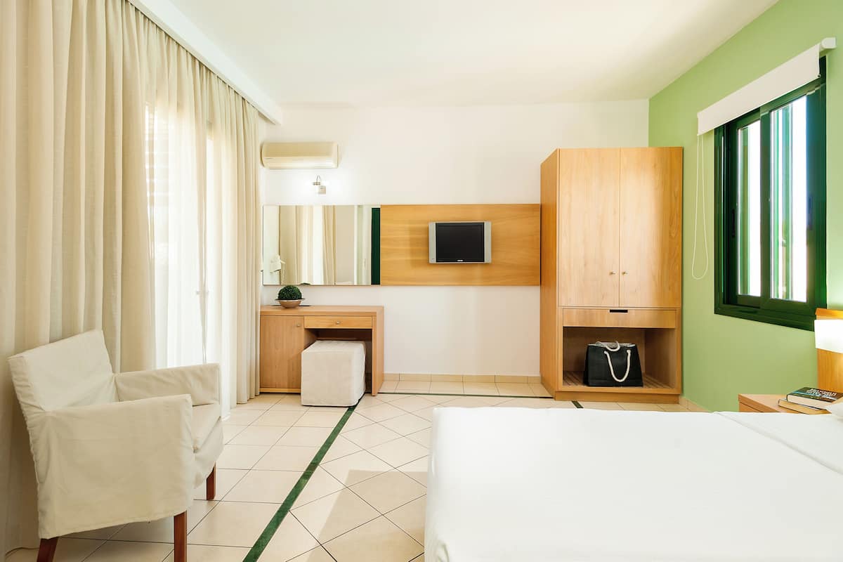 A hotel room with a bed, a desk with a chair, a TV, a wardrobe, and a window with curtains.