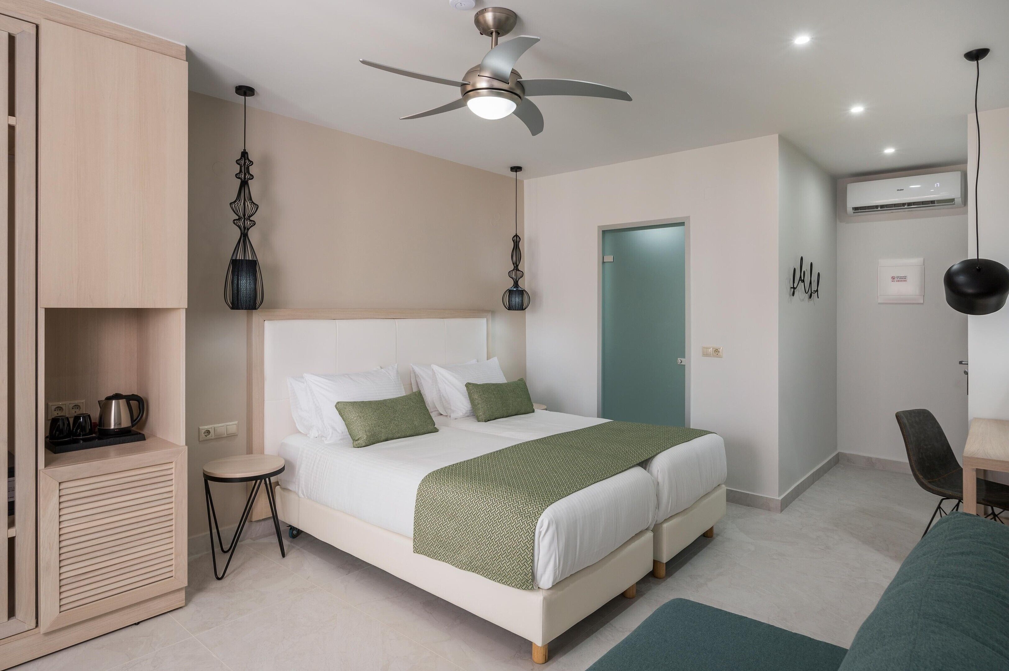 A hotel room with a bed, a desk, a chair, a ceiling fan, and an air conditioning unit.