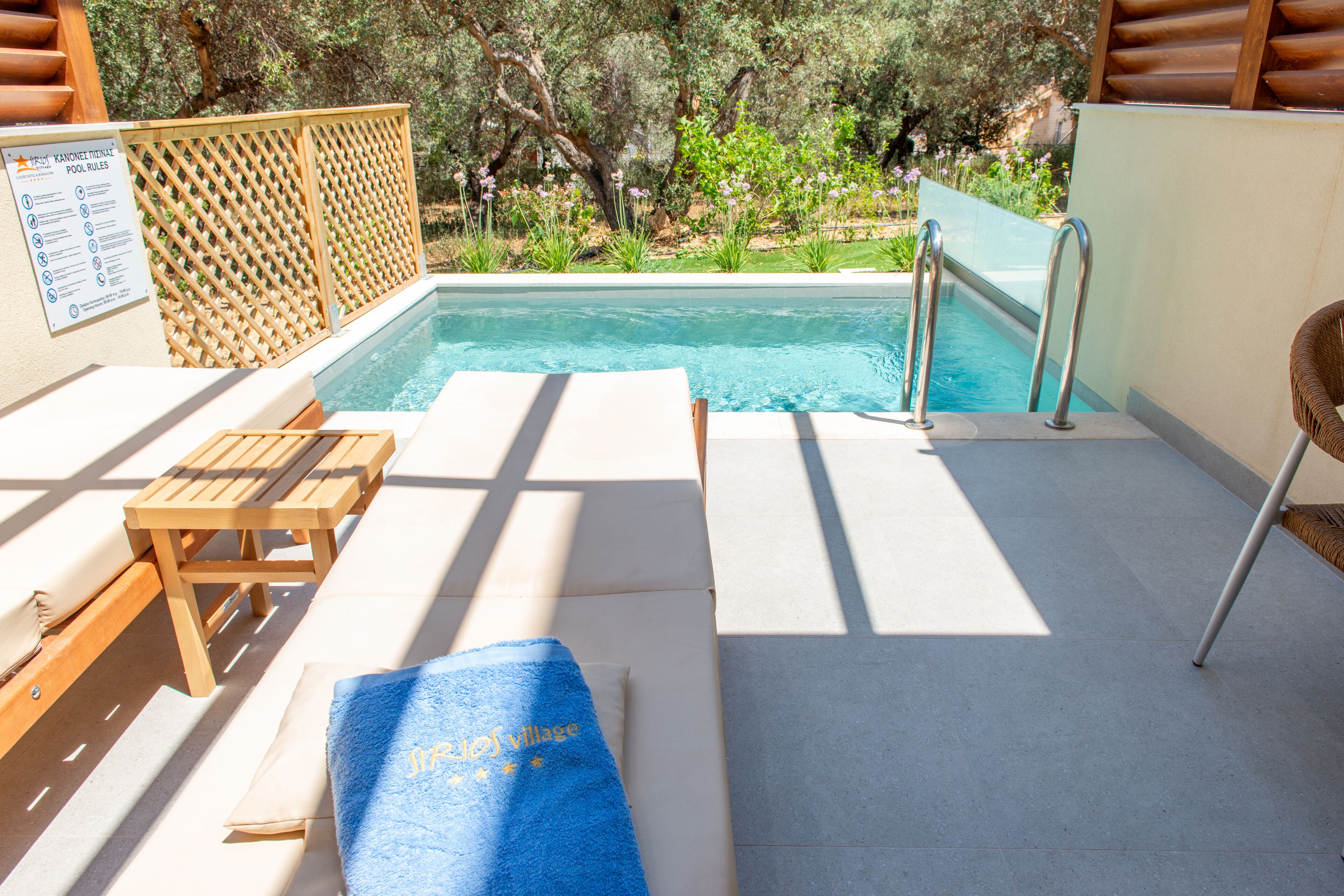 A poolside area with a wooden bench, lounge chairs, and a blue towel.