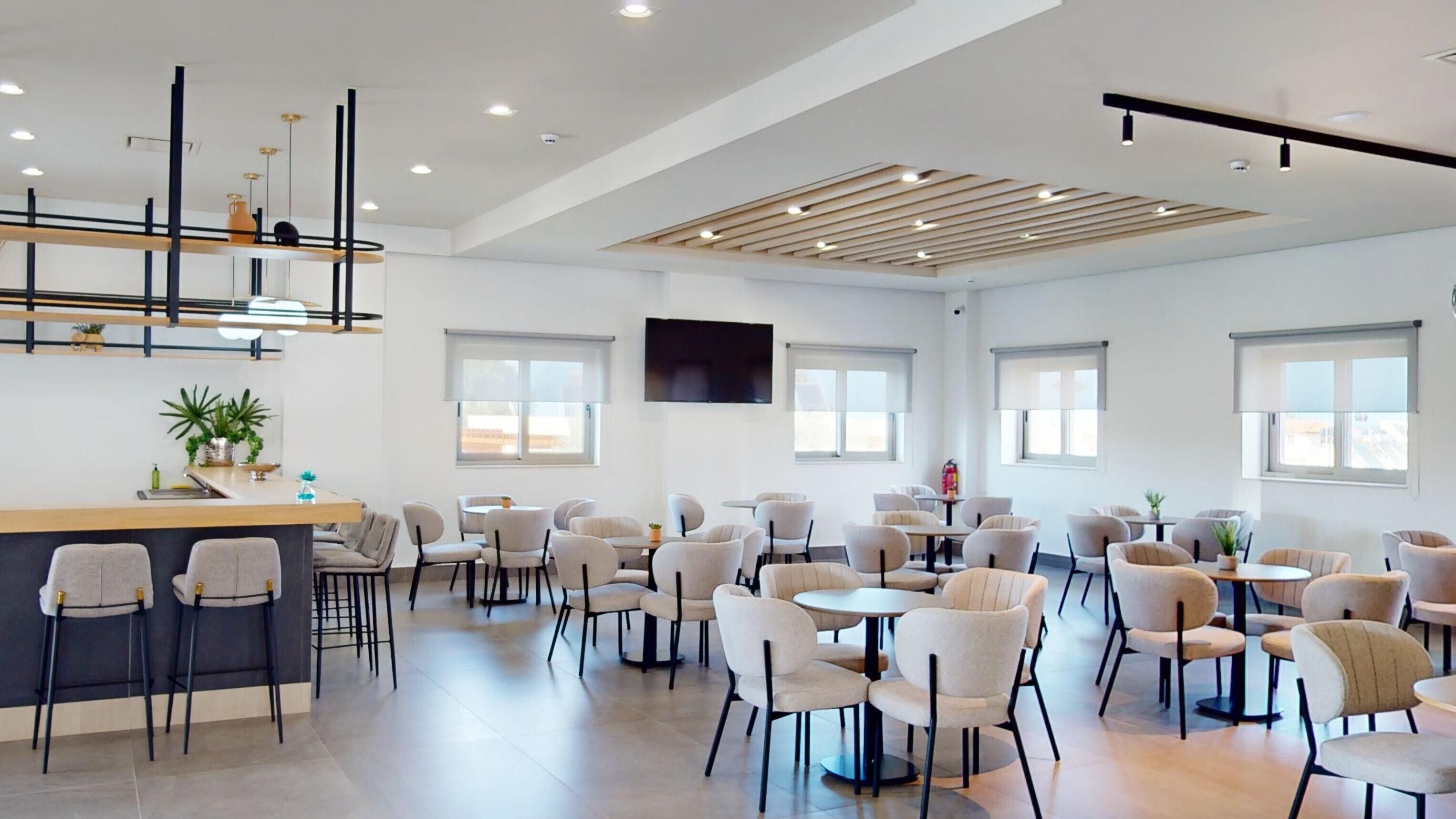 A modern dining area with multiple tables and chairs, a bar counter, and a flat-screen TV mounted on the wall.