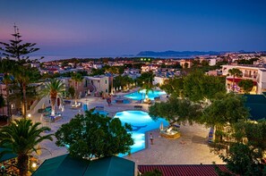 A resort with multiple swimming pools, palm trees, and a view of the sea and distant mountains. - Sirios Village Hotel & Bungalows - All Inclusive (Chania)