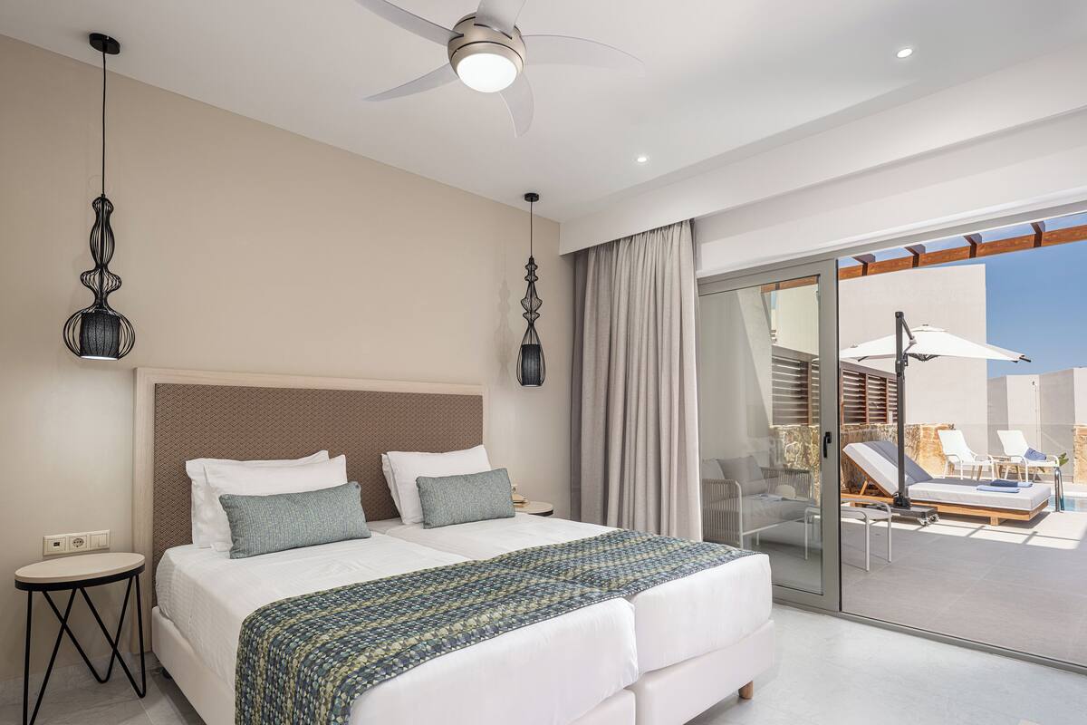 A modern hotel room with a large bed, a ceiling fan, and a view of the outdoor pool area.