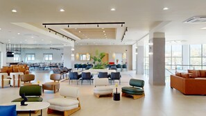 A spacious hotel lobby with multiple seating areas, a central plant, and large windows. - Sirios Village Hotel & Bungalows - All Inclusive (Chania)