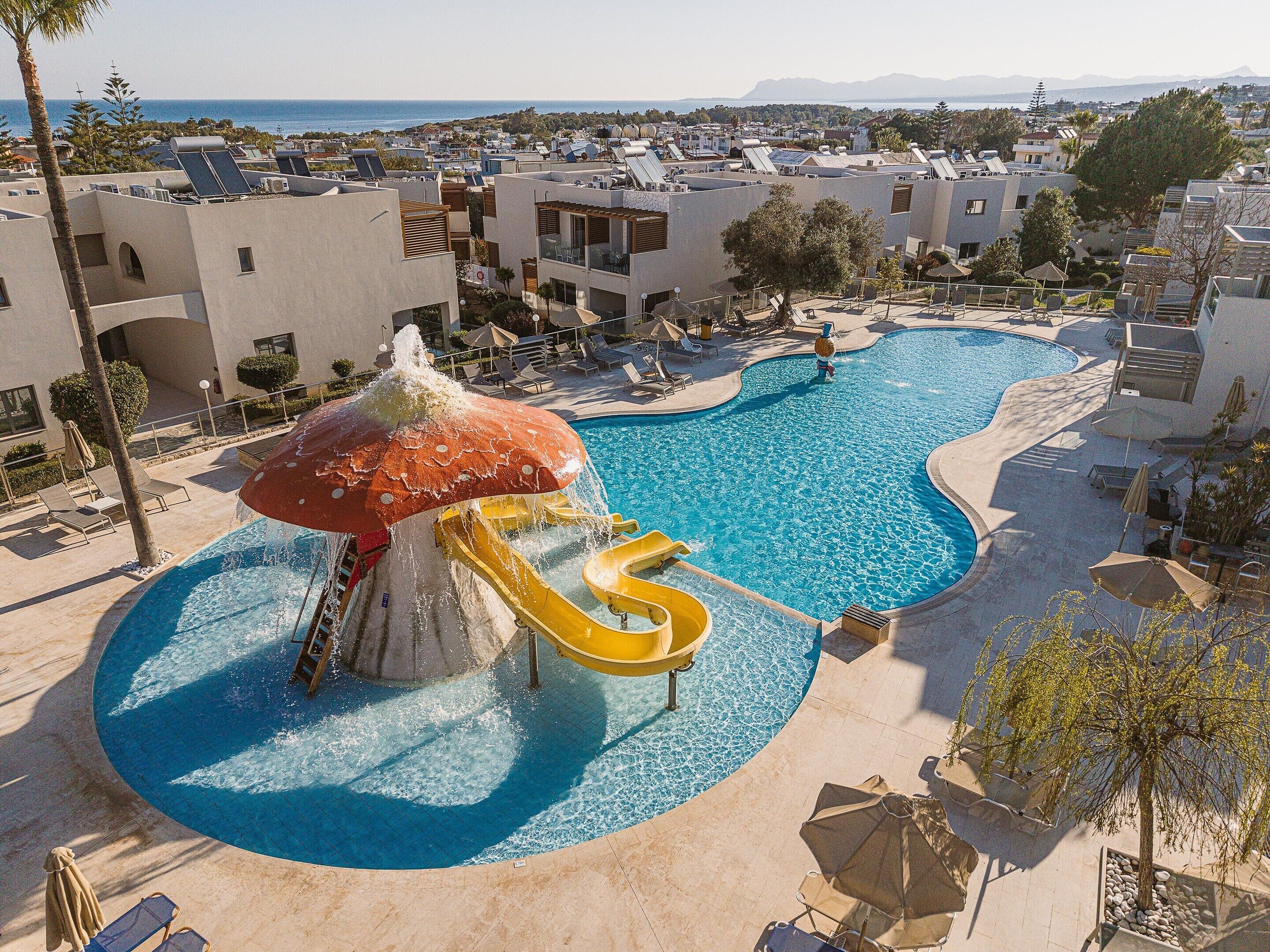 A resort pool with a water slide and a view of the surrounding buildings.