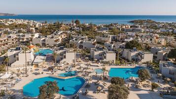 Ein Resort mit mehreren Schwimmbecken, Liegestühlen und Blick auf das Meer.