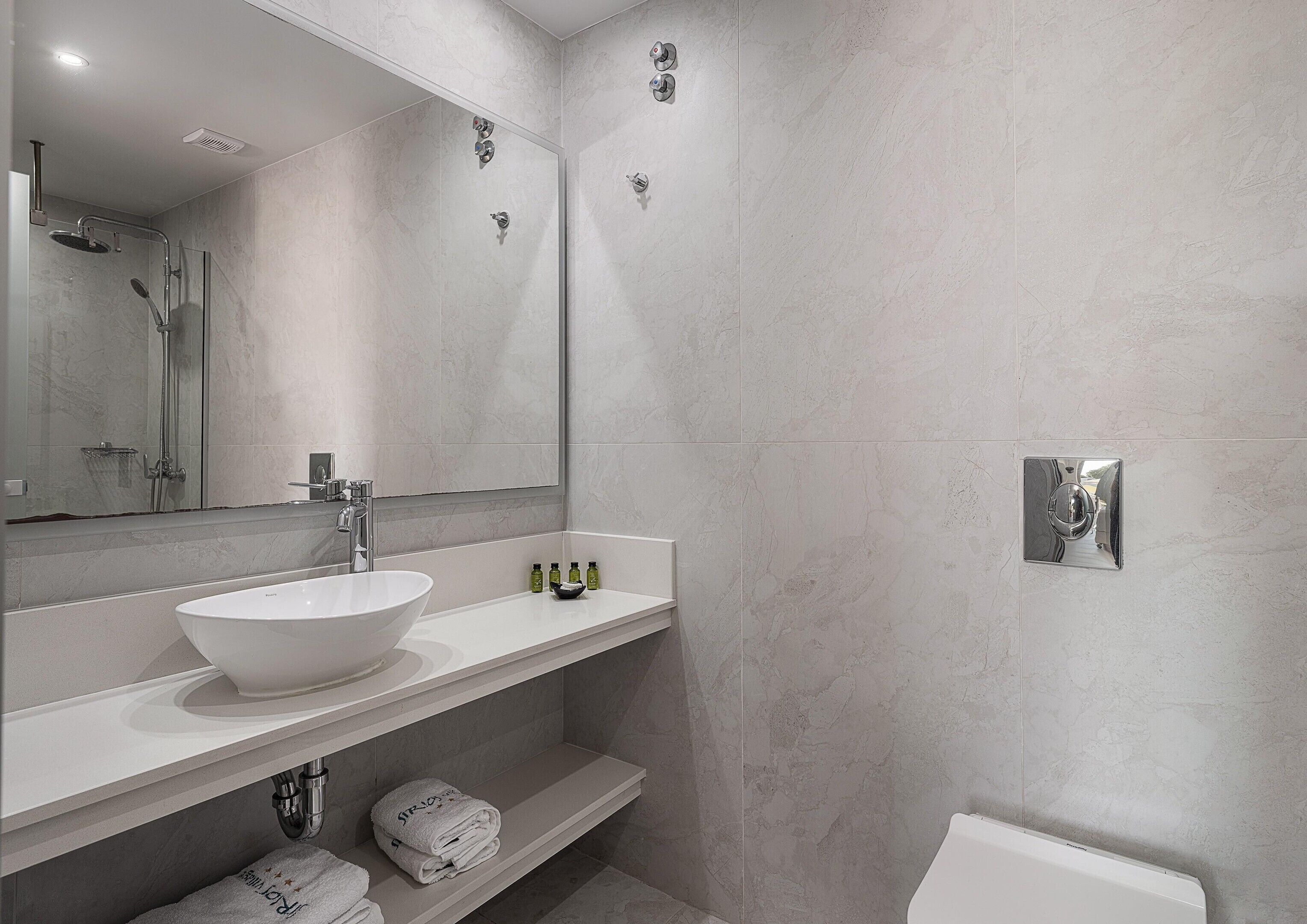 A modern bathroom with a white sink, a mirror, a shower, and a toilet.