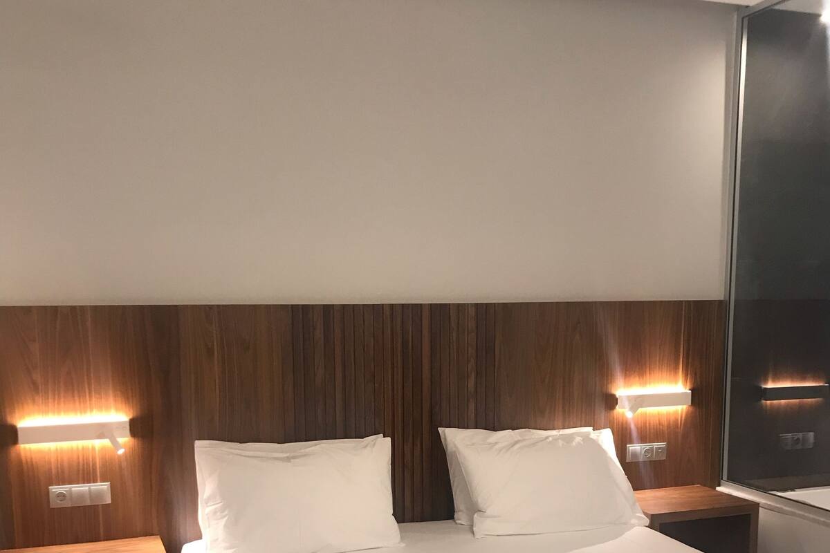 A hotel room with a large bed, two bedside tables, and wall-mounted lamps.