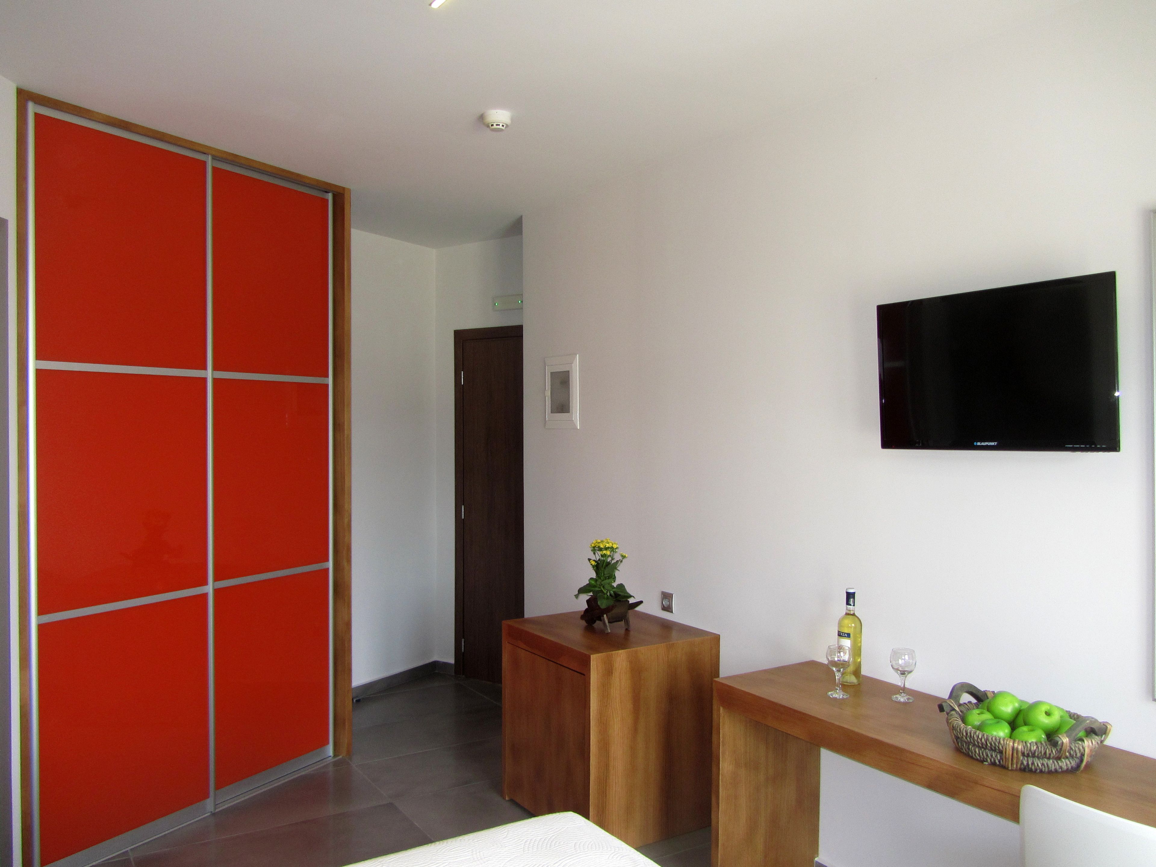 A modern room with a wooden desk, a television, a red partition, and a basket of green apples.