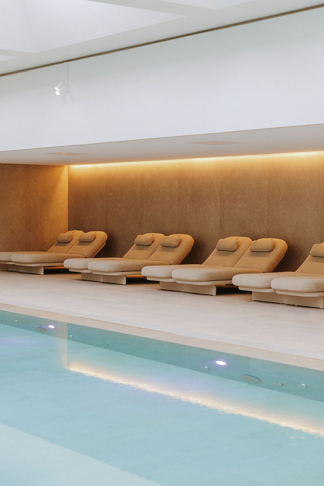 Un área junto a la piscina con sillones de descanso y una tira de luz cálida a lo largo de la pared.