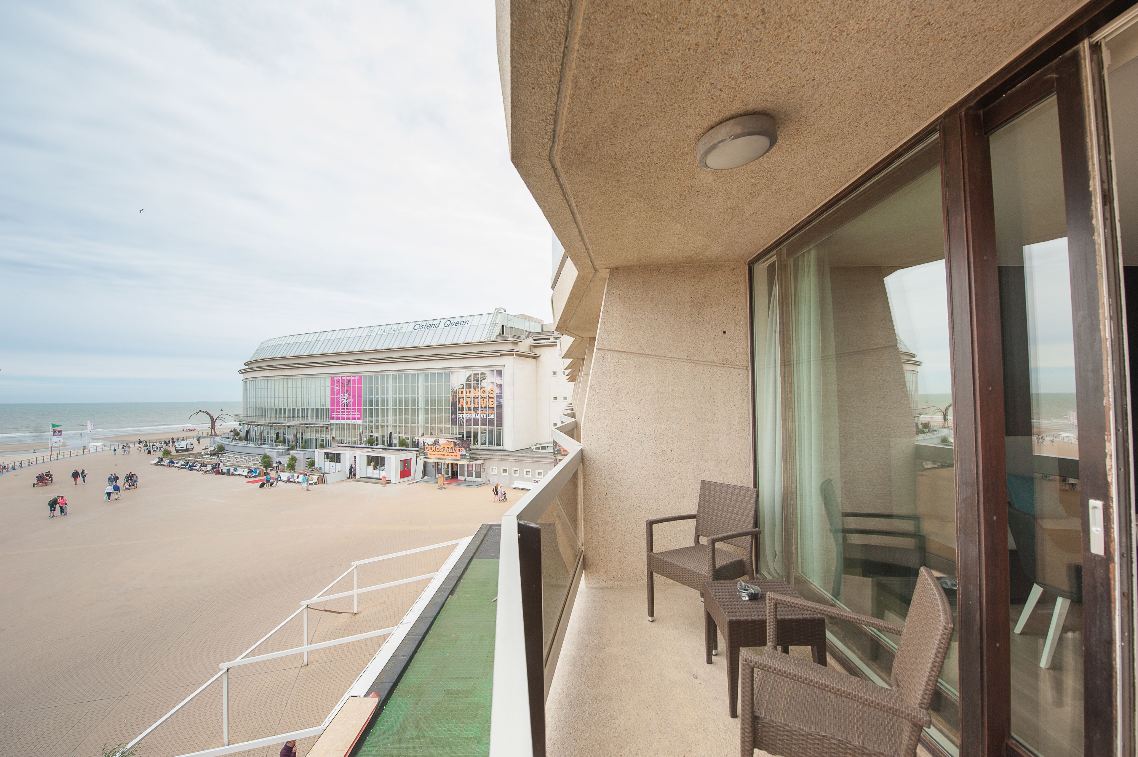 Een balkon met rieten stoelen en uitzicht op het strand en een hotelgebouw.