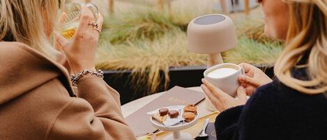 Two people seated at an outdoor table with a dessert plate, a cup, and a smartphone.