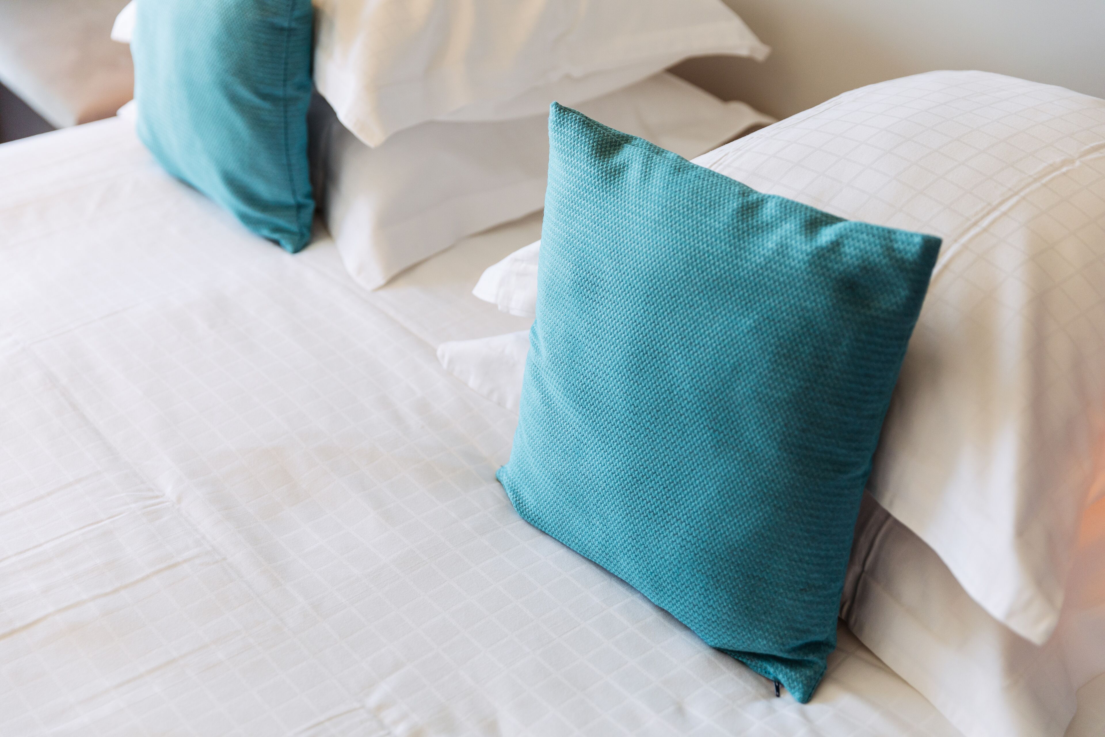 Een net opgemaakt bed met witte lakens en teal kussens.