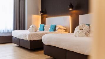 Two beds with white linens and teal pillows, a dark headboard, and a window with curtains.