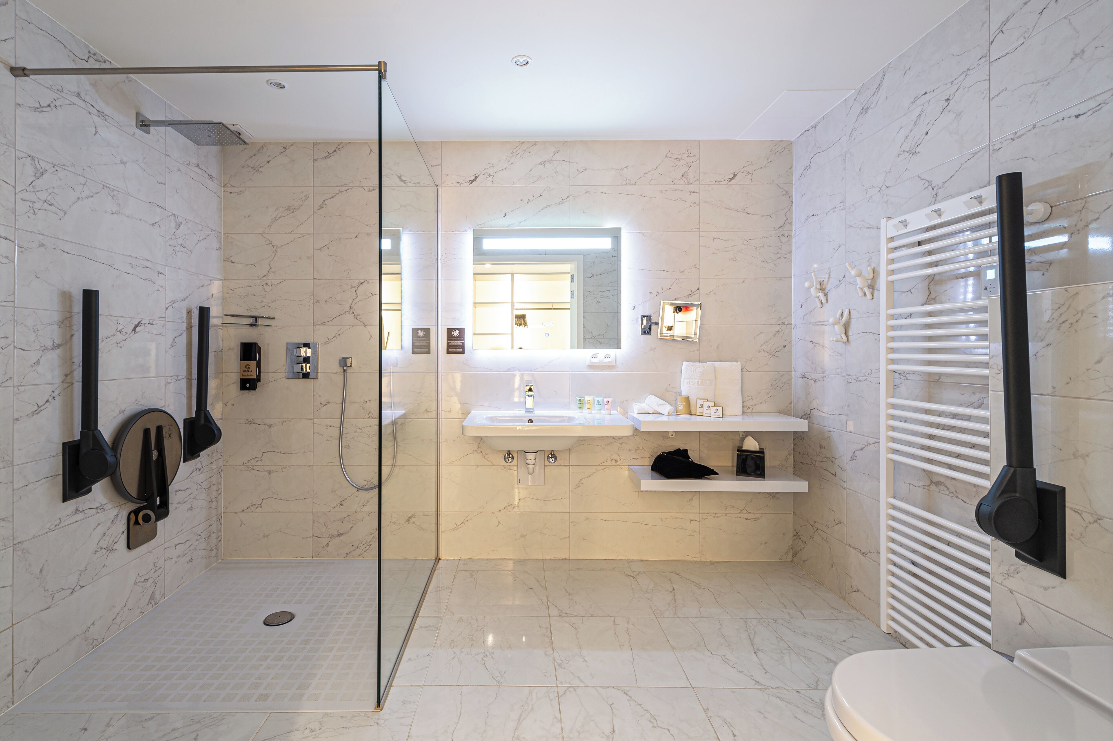 Un baño moderno con cabina de ducha de vidrio, un espejo grande, un lavabo con tocador y un perchero para toallas.