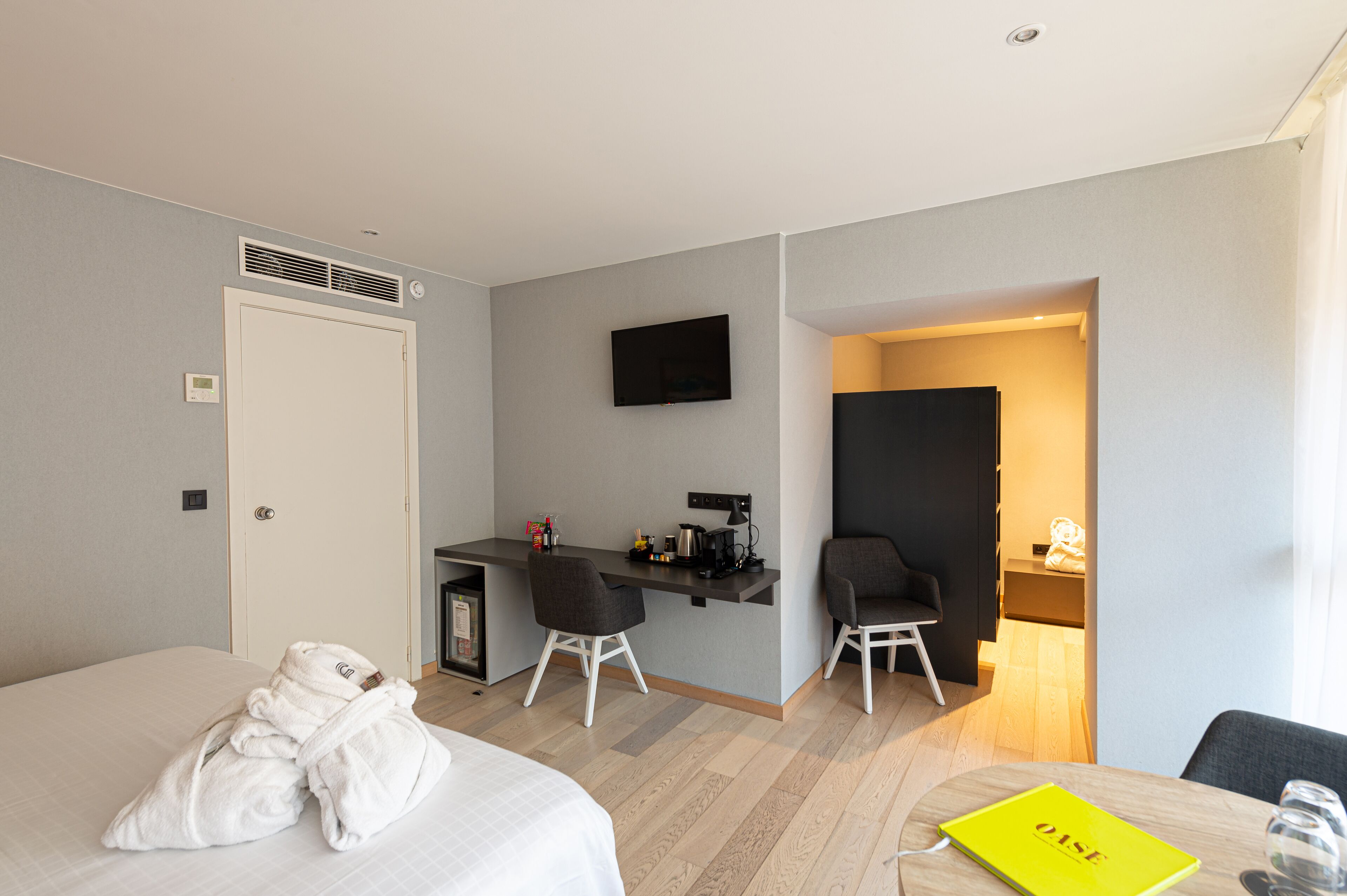 A hotel room with a bed, a desk with a chair, a TV, and a small kitchenette.