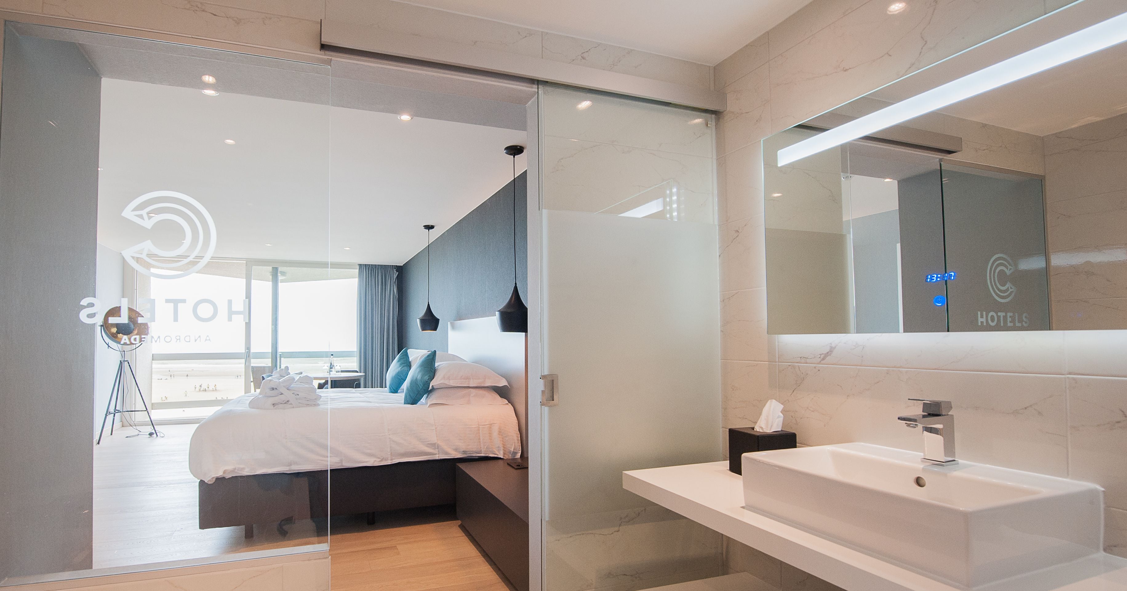 A modern hotel room with a bed, bedside table, and a large mirror.