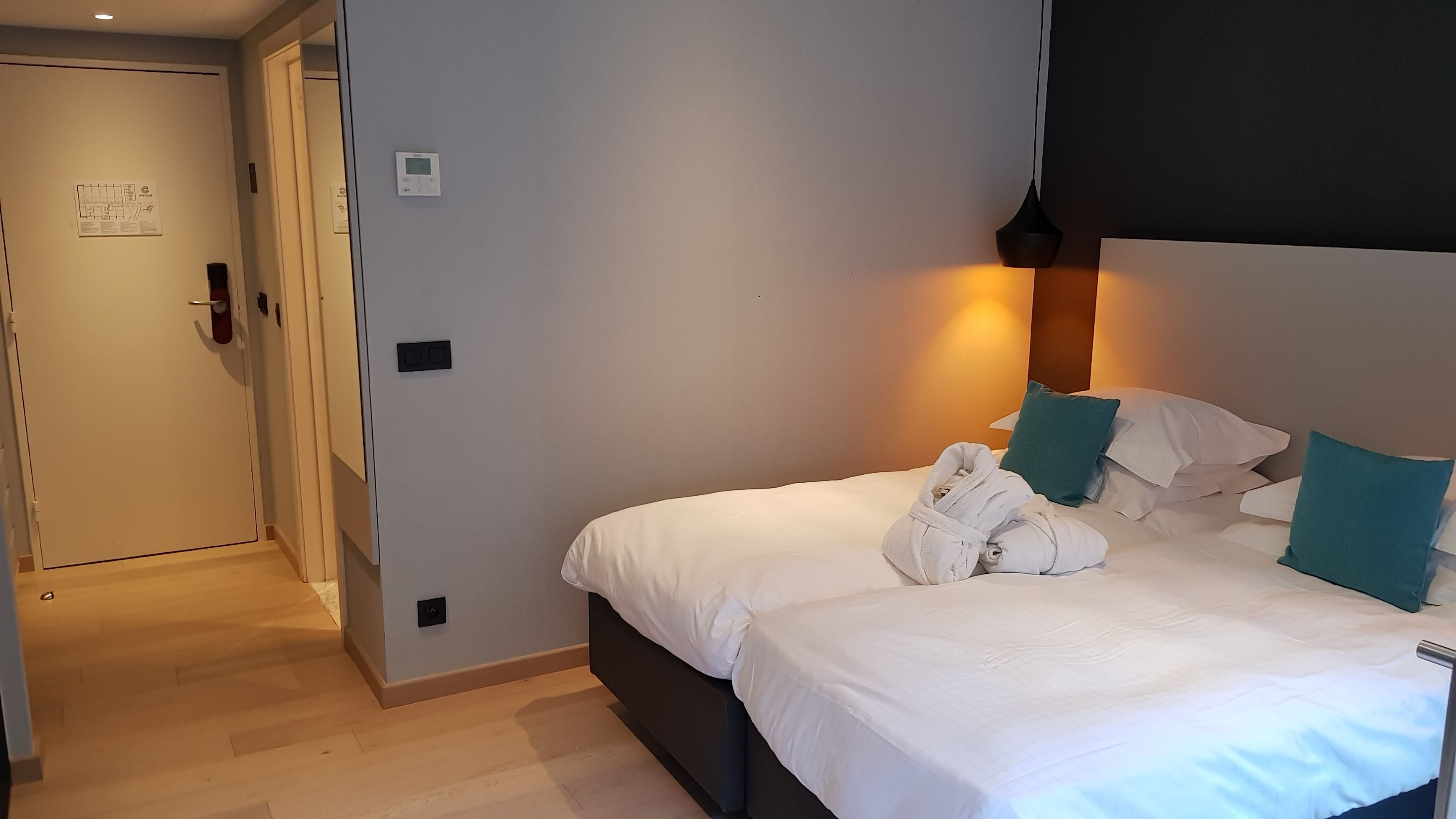 Une chambre d’hôtel avec un lit, du linge de lit blanc, des oreillers turquoise et un peignoir posé sur le lit.