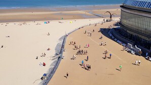 Une plage avec une promenade en arc de cercle, une plage de sable et un grand bâtiment doté d’un toit incurvé.